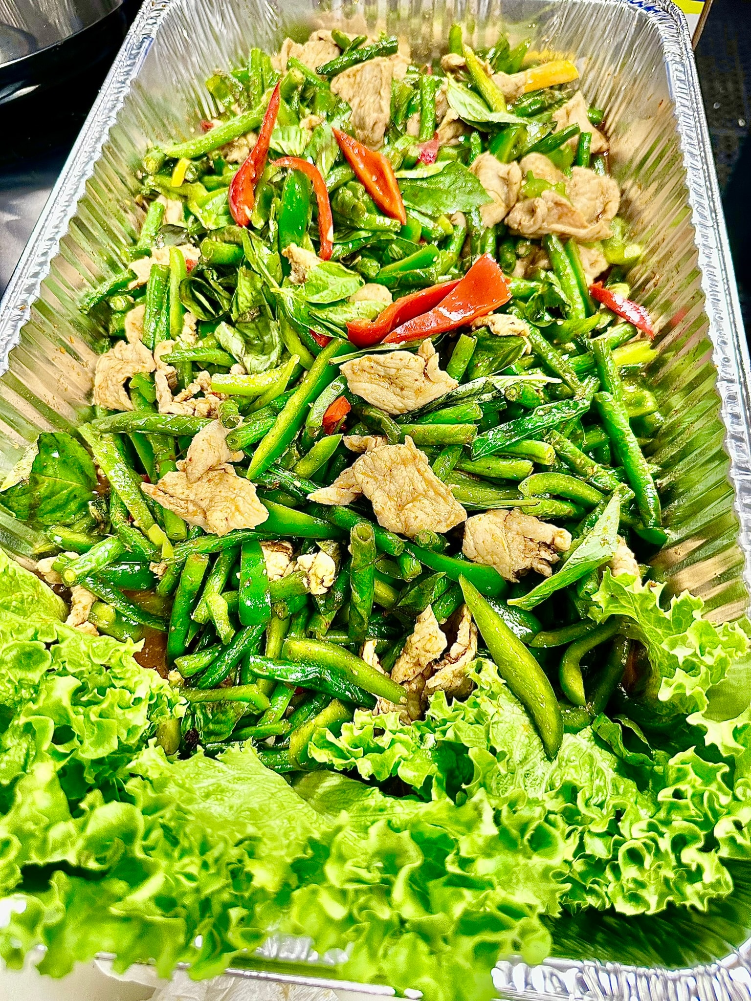 Catering tray of Thai green bean stir fry with pork, red peppers and lettuce garnish