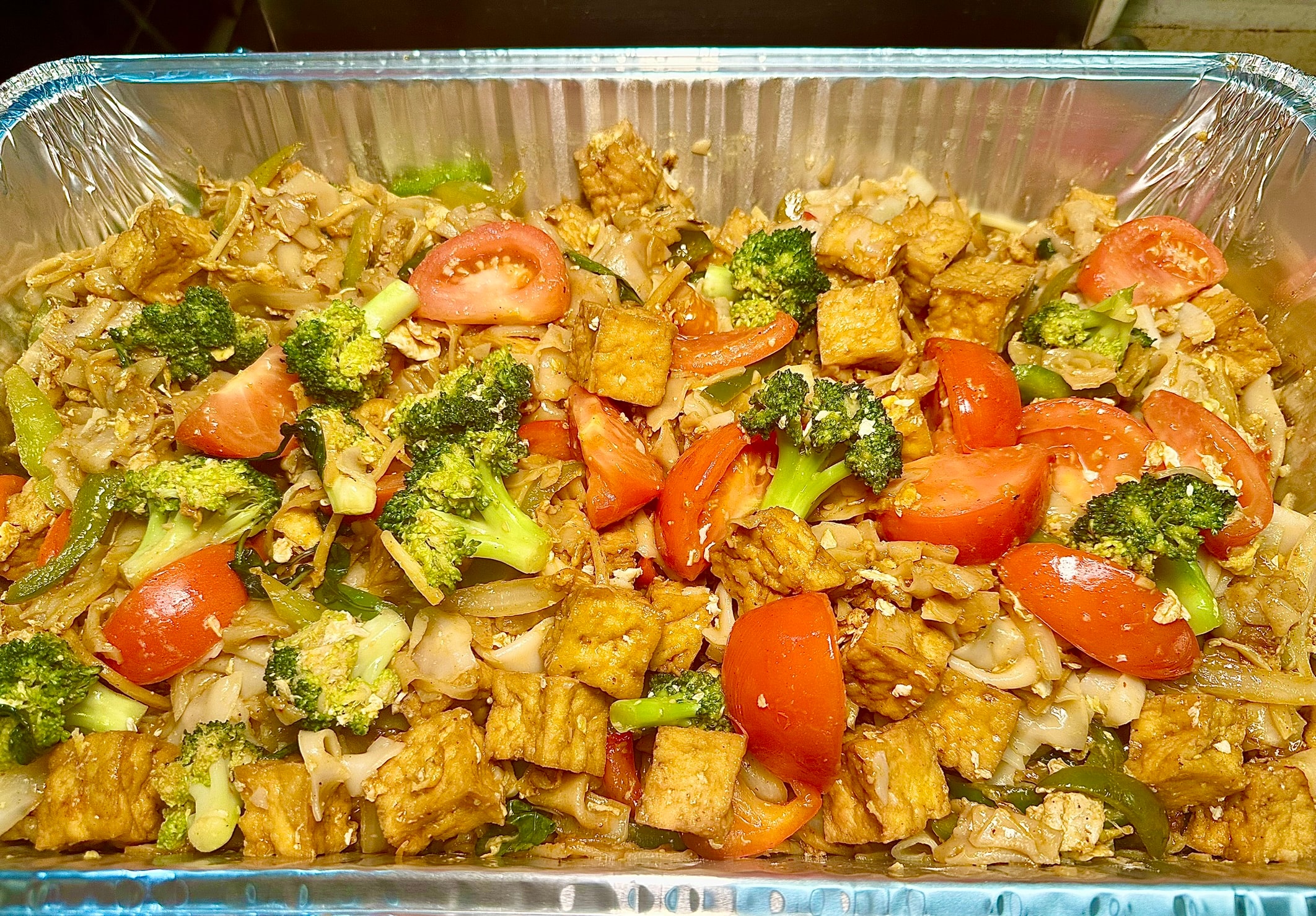 Large catering tray of Kee Mao drunken noodles with wide rice noodles, chicken, tomatoes and broccoli