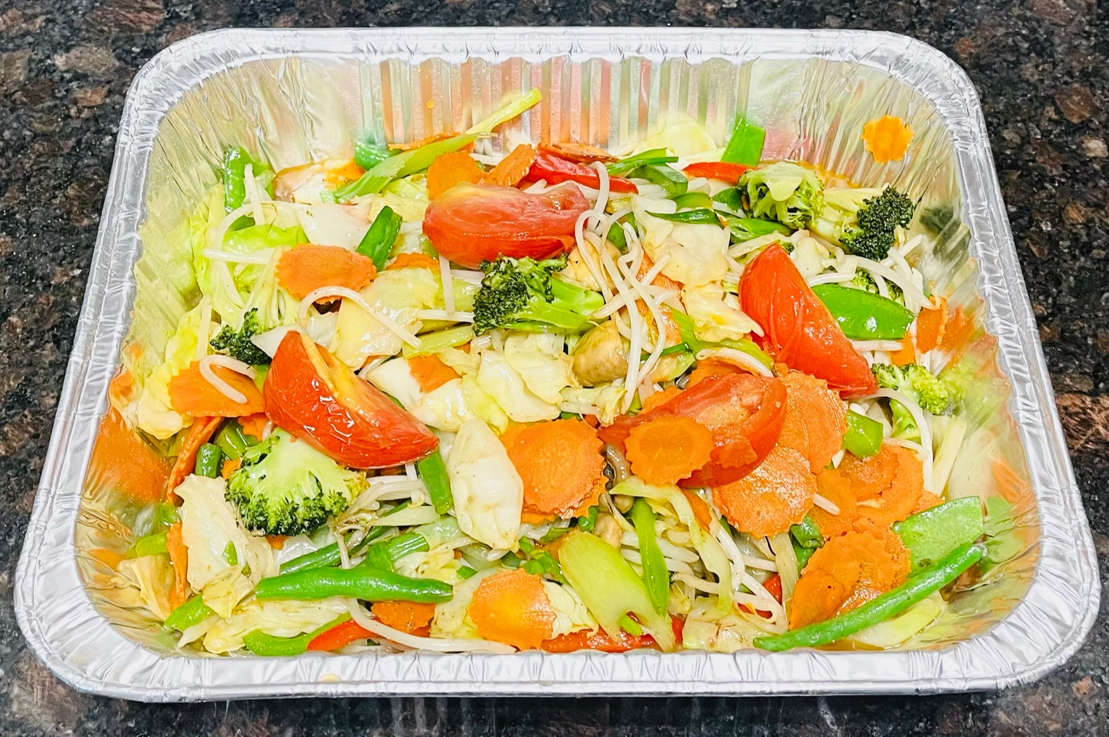 Small catering tray of mixed vegetable stir fry with carrots, broccoli, bean sprouts, snap peas and tomatoes