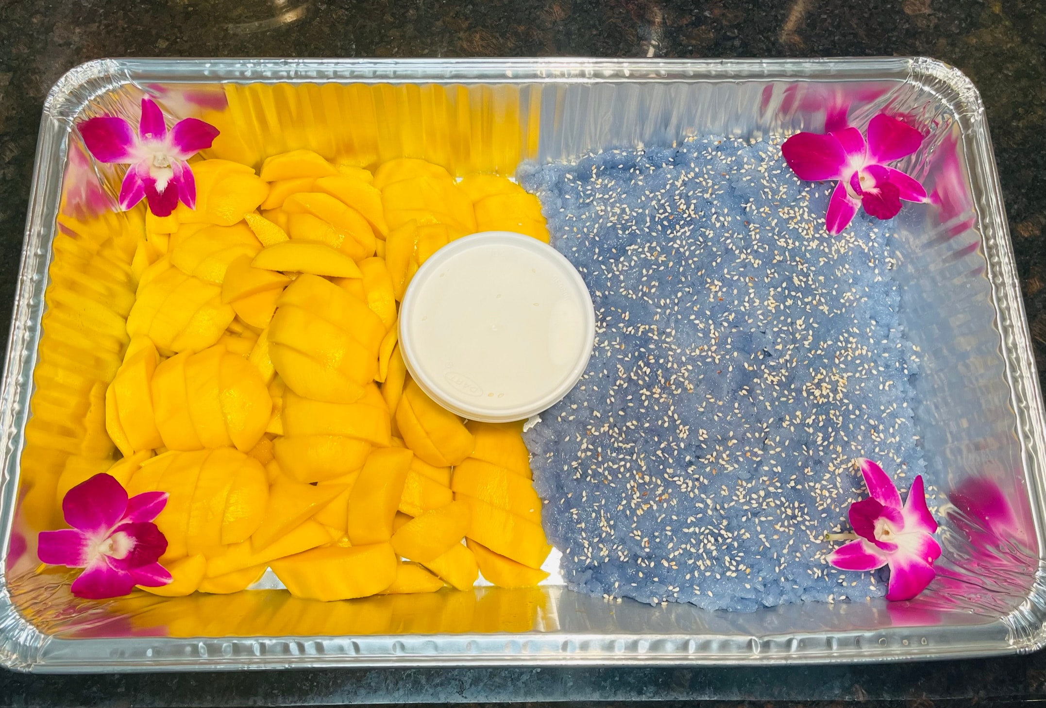 Decorative tray with yellow petals, magenta orchids and a white bowl for catering display