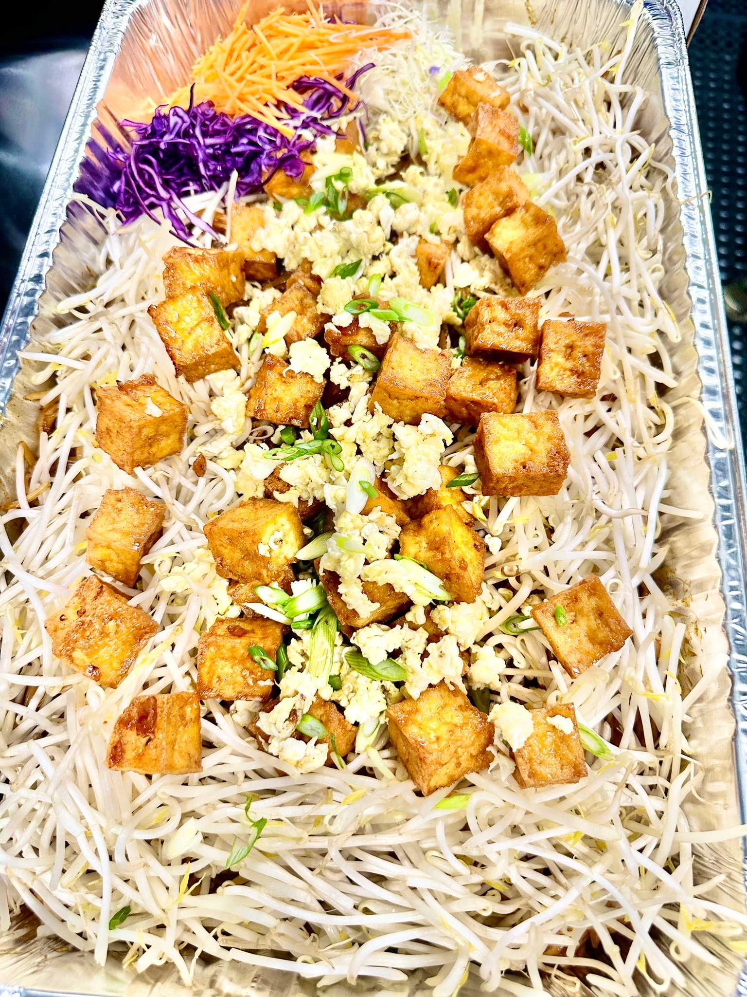 Catering tray of Pad Thai with crispy tofu, bean sprouts, egg, green onions, shredded carrots and purple cabbage
