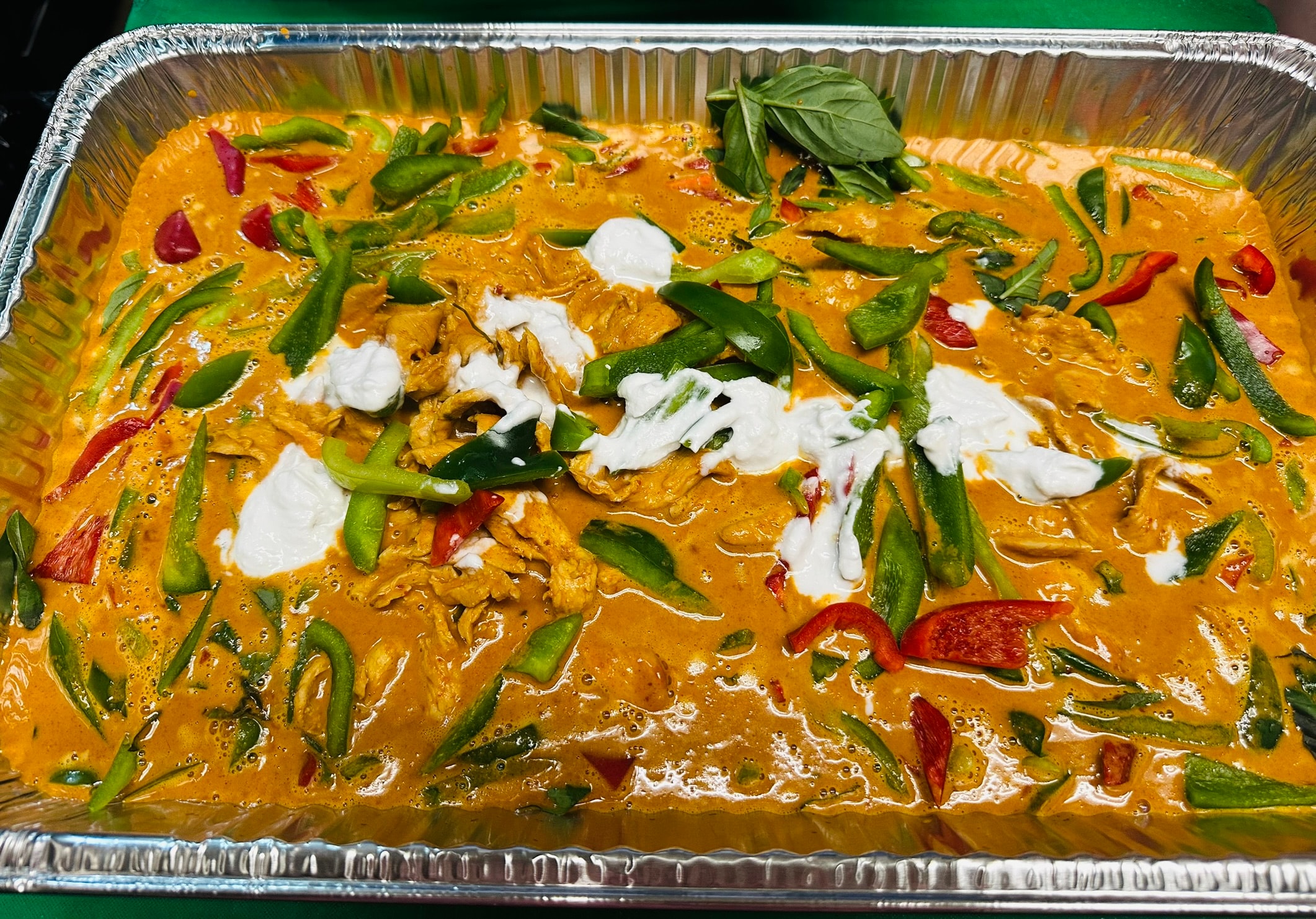 Large catering tray of Panang curry with chicken, green and red peppers, coconut cream and basil