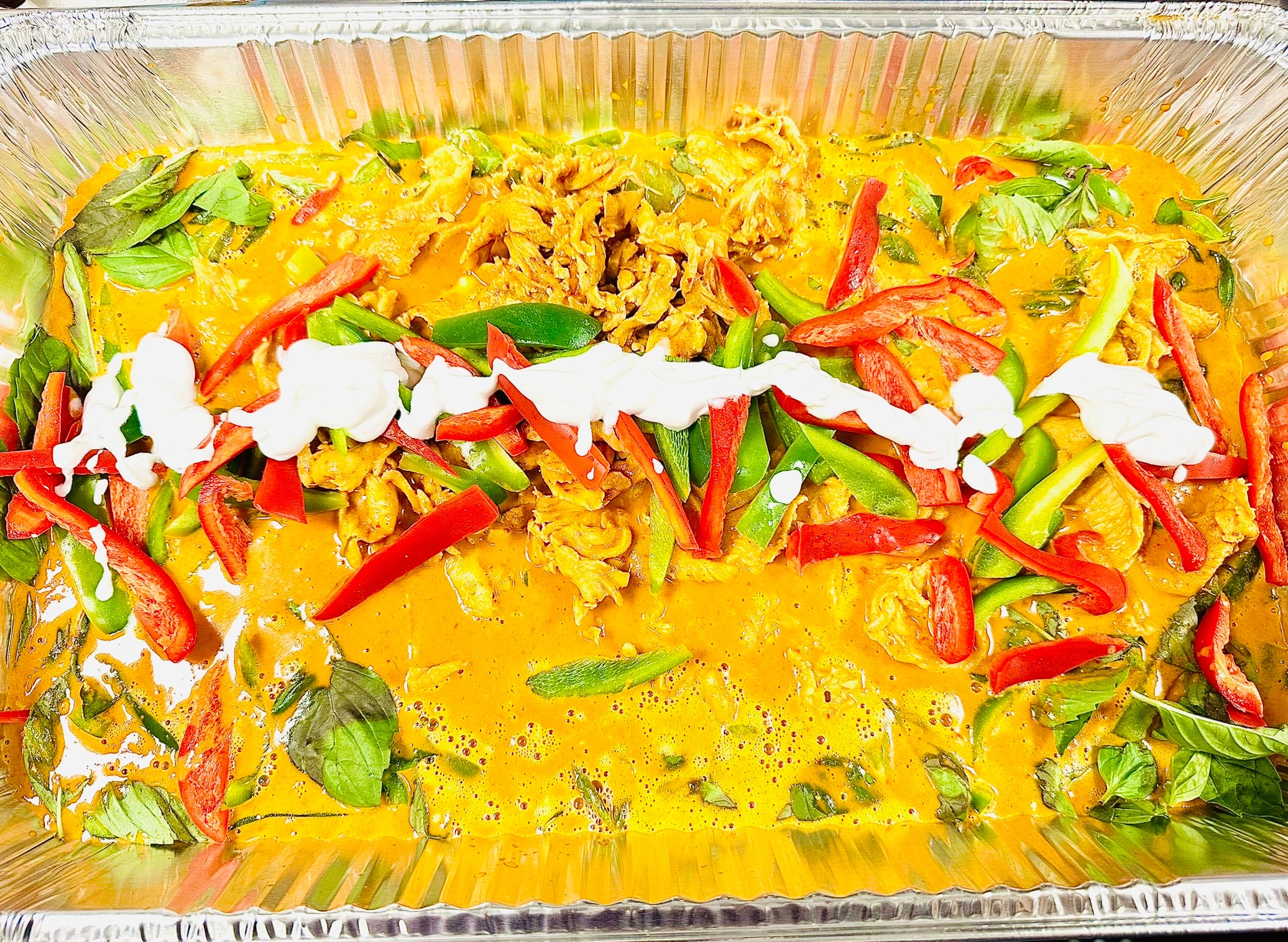 Large catering tray of golden Panang curry with chicken, red and green peppers, basil and coconut cream drizzle
