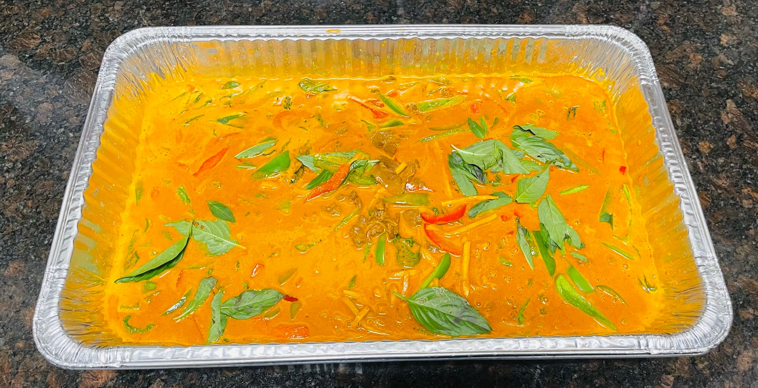 Large catering tray of red curry with basil leaves and chili peppers
