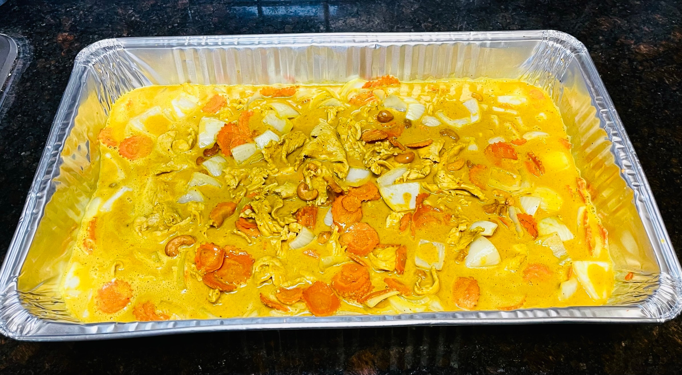 Large catering tray of yellow curry with chicken, carrots and onions