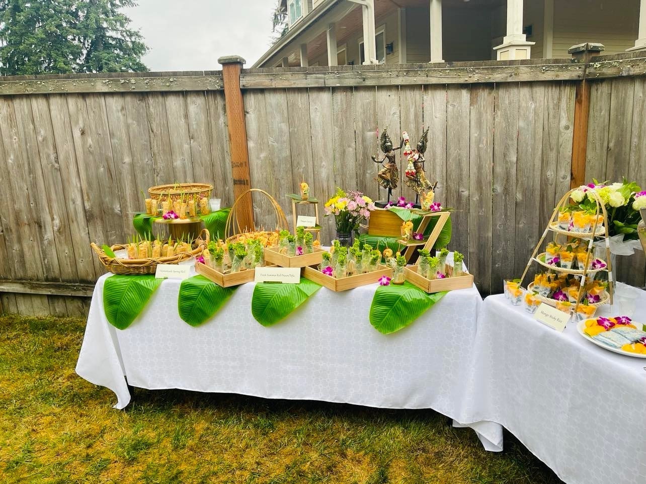 Full outdoor appetizer table with spring rolls, summer rolls and tropical flowers